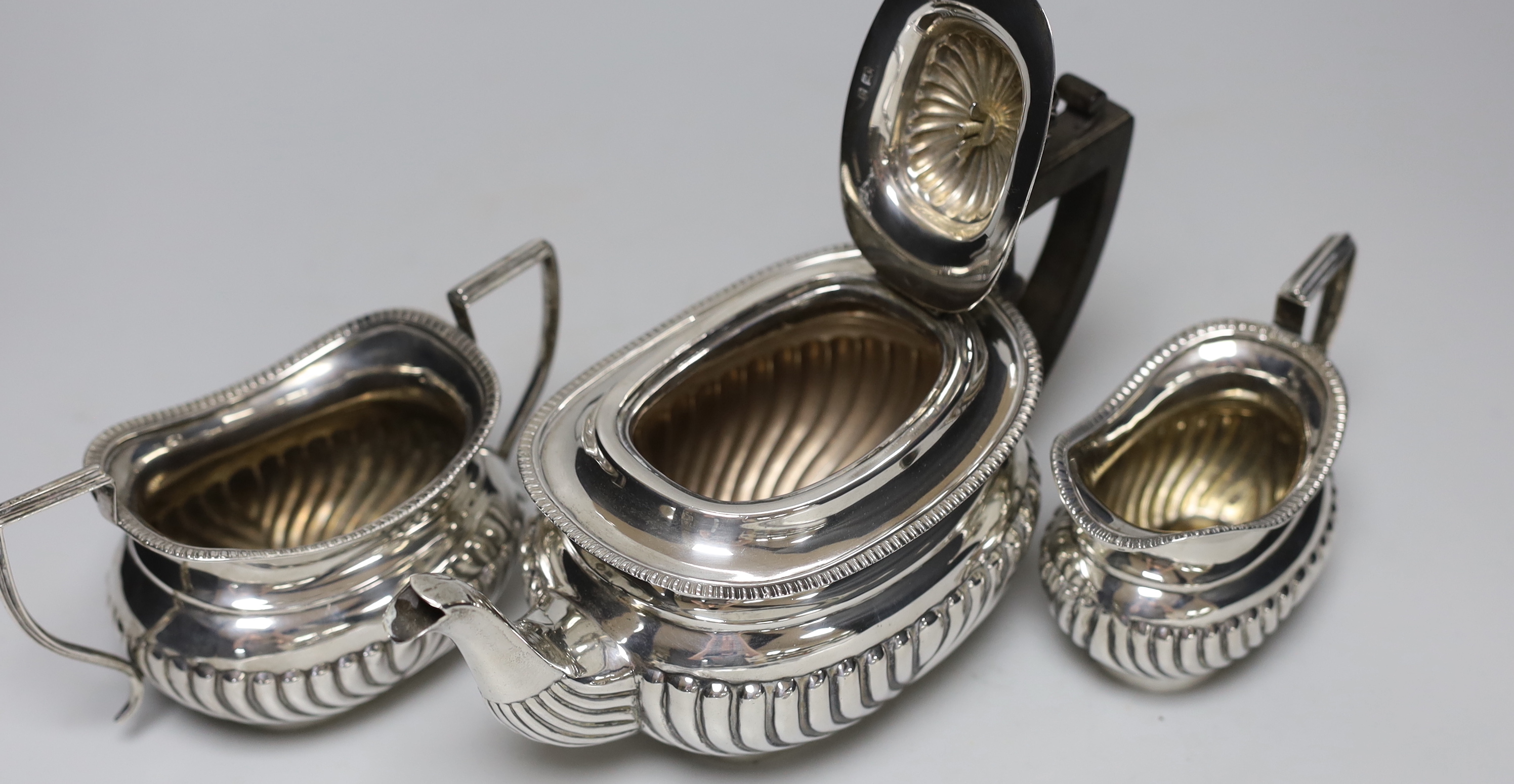 A late Victorian demi-fluted silver three piece tea set, Birmingham, 1899/1900 and a later small silver toastrack, gross weight 24.1oz.